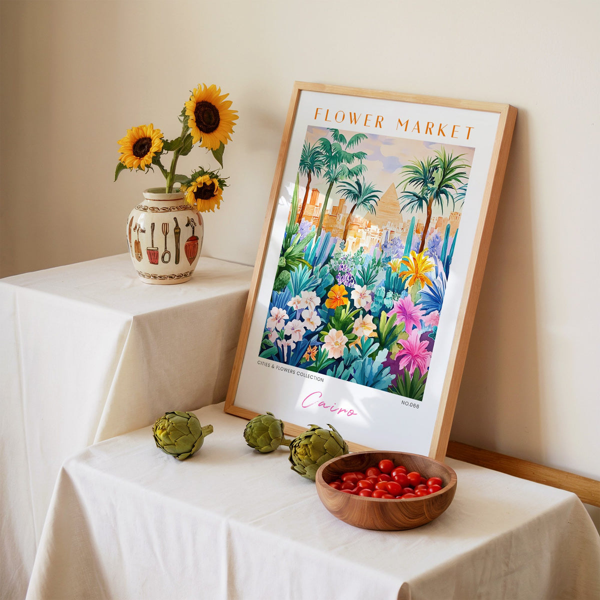 Cairo flower market print in an oak frame leaning on a linen-draped table beside a vase of sunflowers