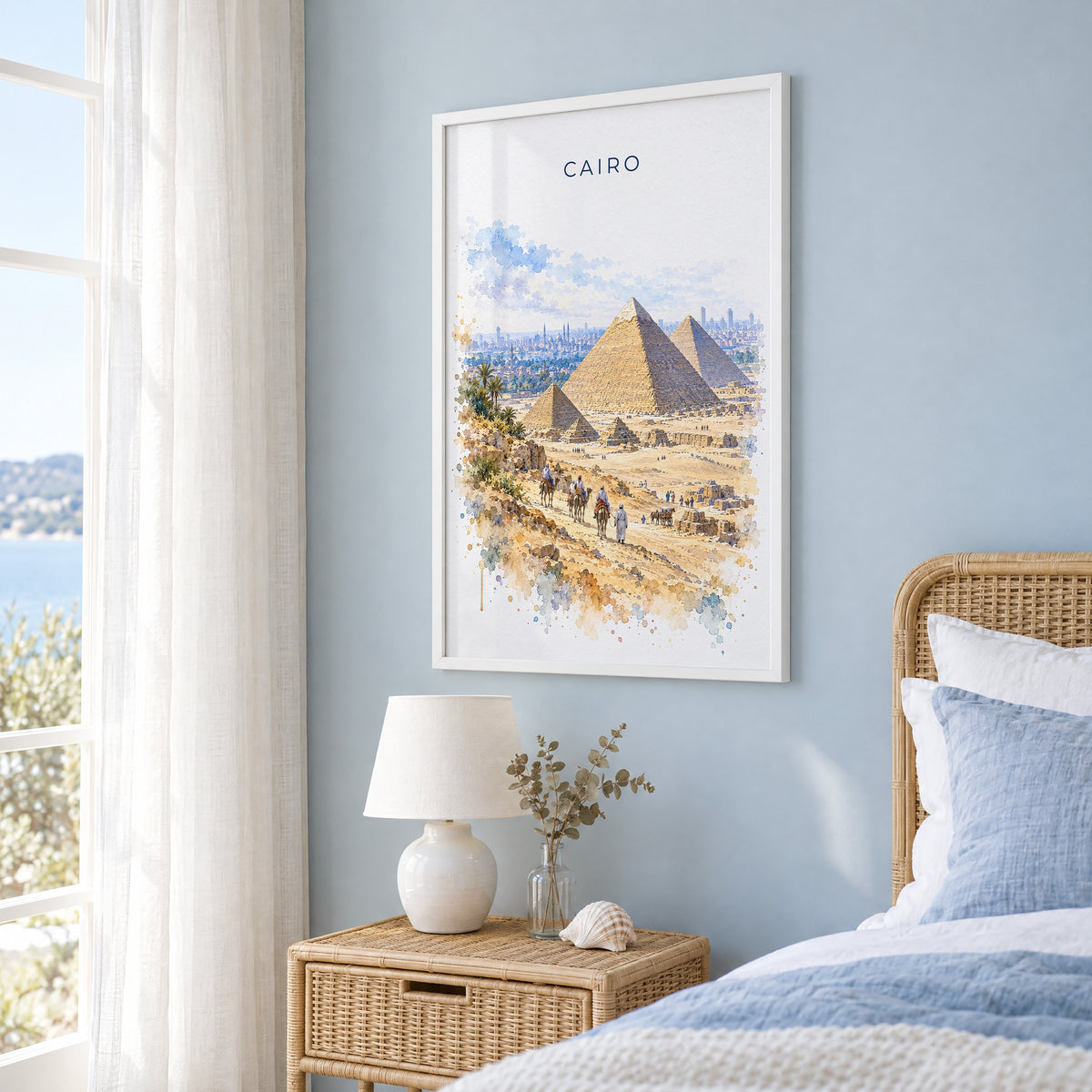 Cairo watercolor print in a white frame on a pale blue wall beside a rattan bed in a coastal bedroom