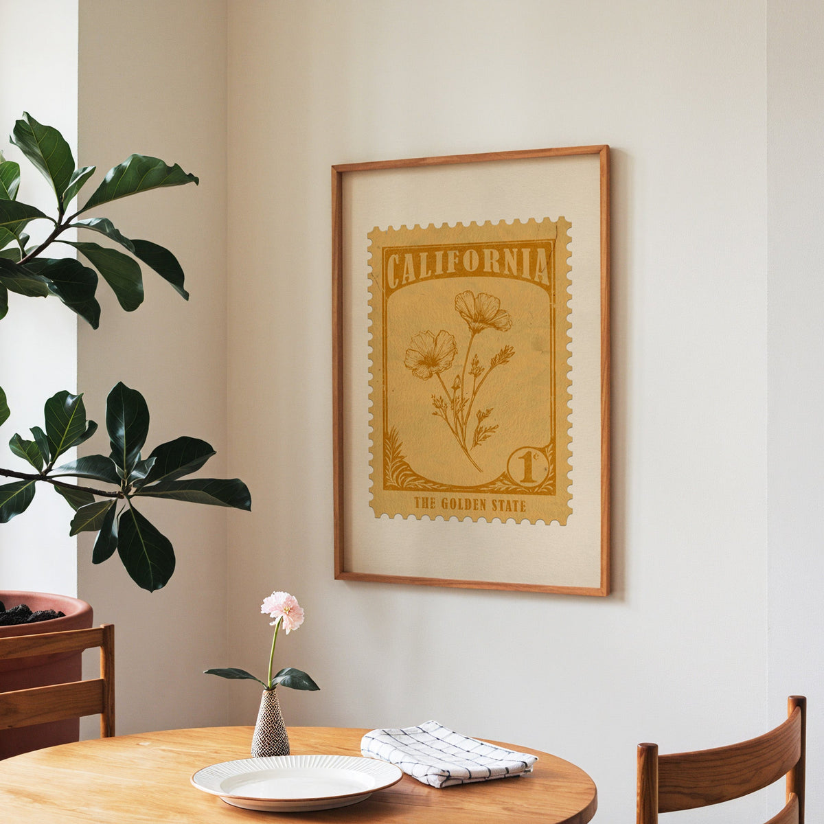 California state flower print framed above a round wooden table with a single bloom in a vase and books