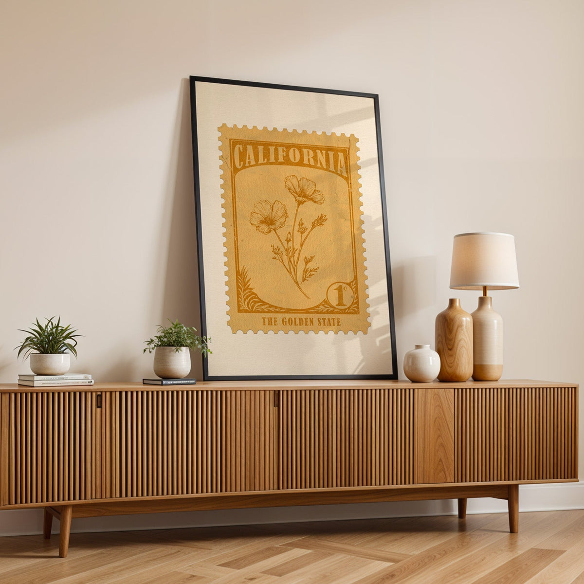 California state flower print in a black frame leaning on a fluted wood credenza with vases and a lamp