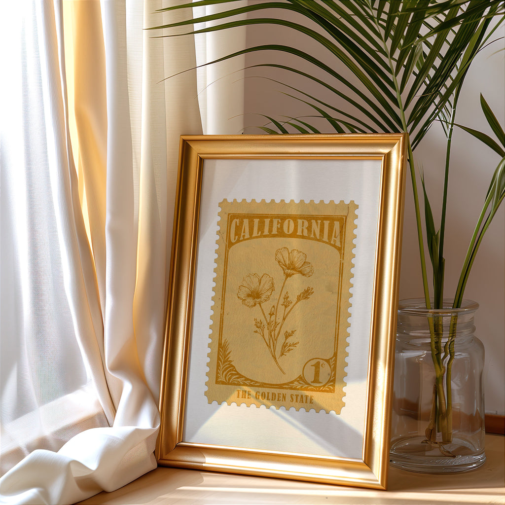 California stamp print in a gold frame leaning by a cream curtain with a palm in a glass jar
