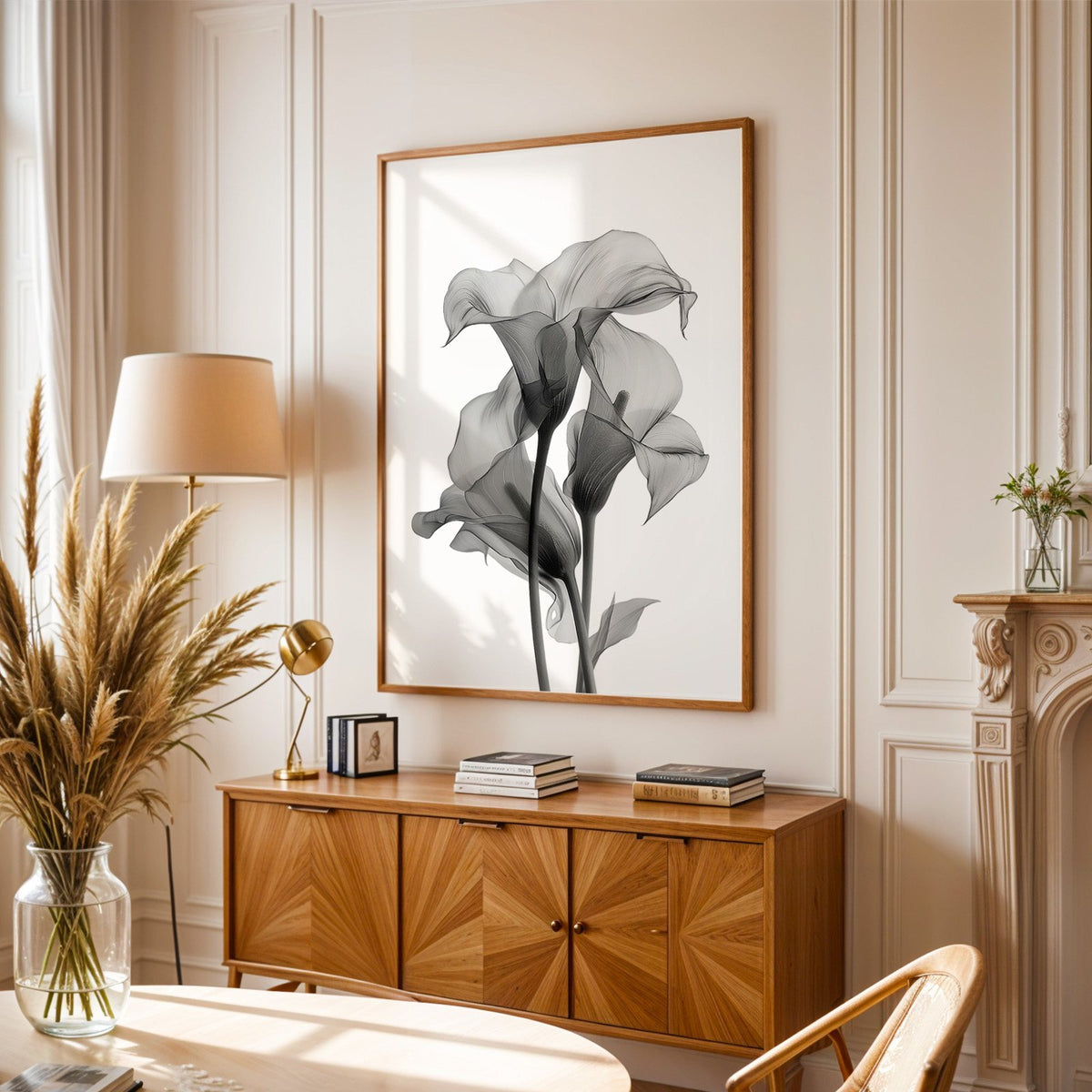 Translucent calla lily X-ray flowers print in an oak frame above a sunburst wood sideboard with pampas grass