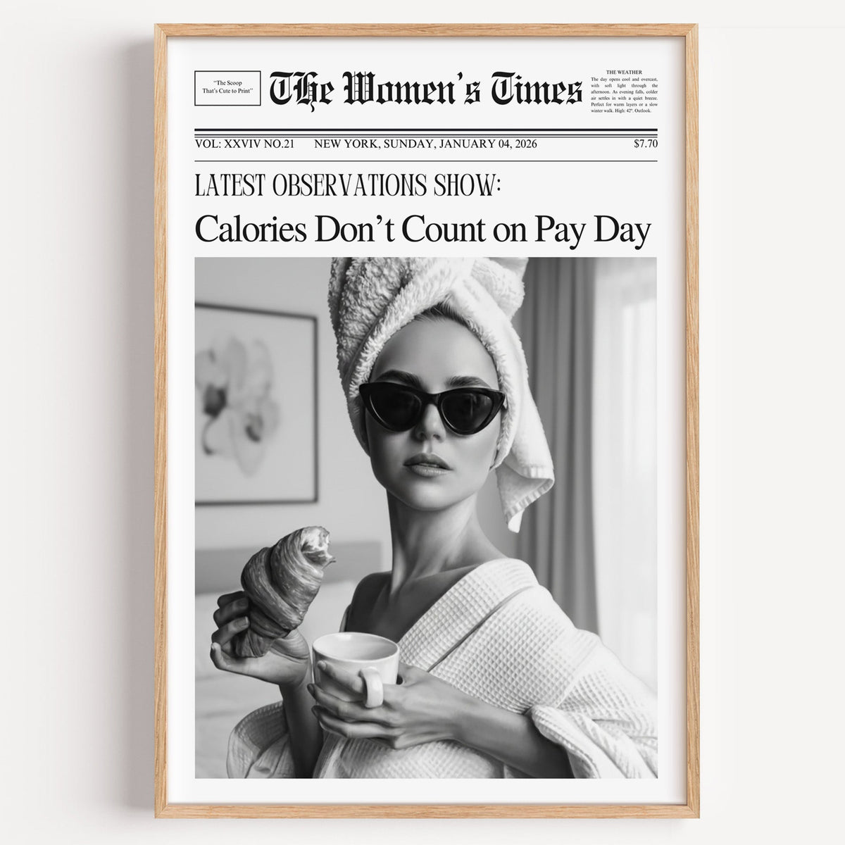 Mock front page with woman eating a croissant print in a light oak frame on a plain white wall