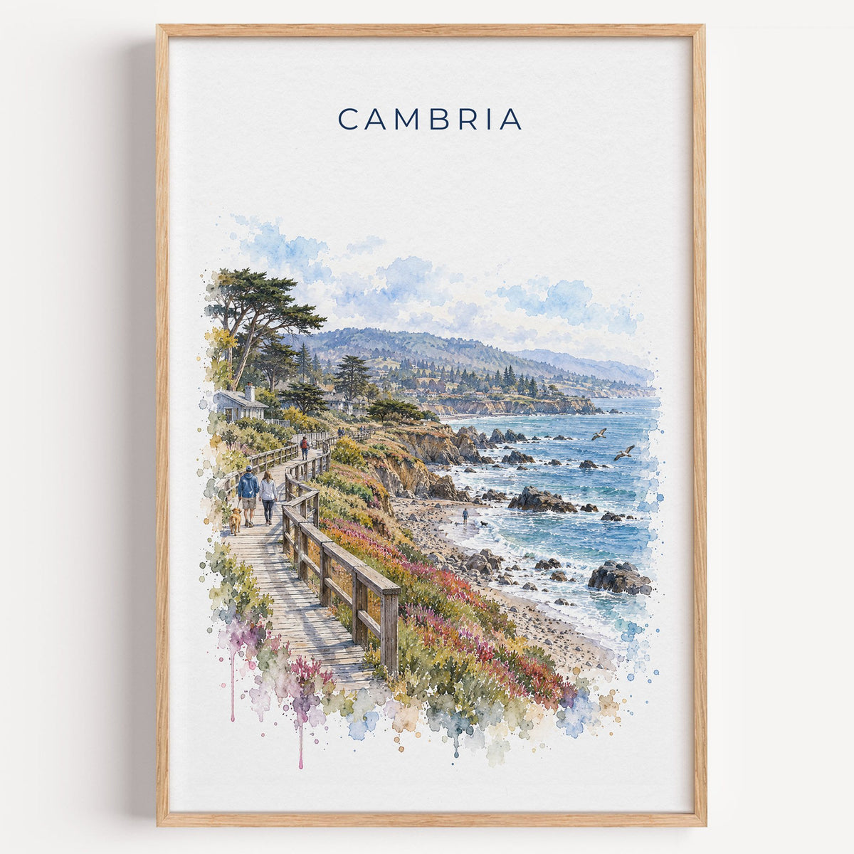 Cambria, California watercolor print in a light oak frame on a plain white wall