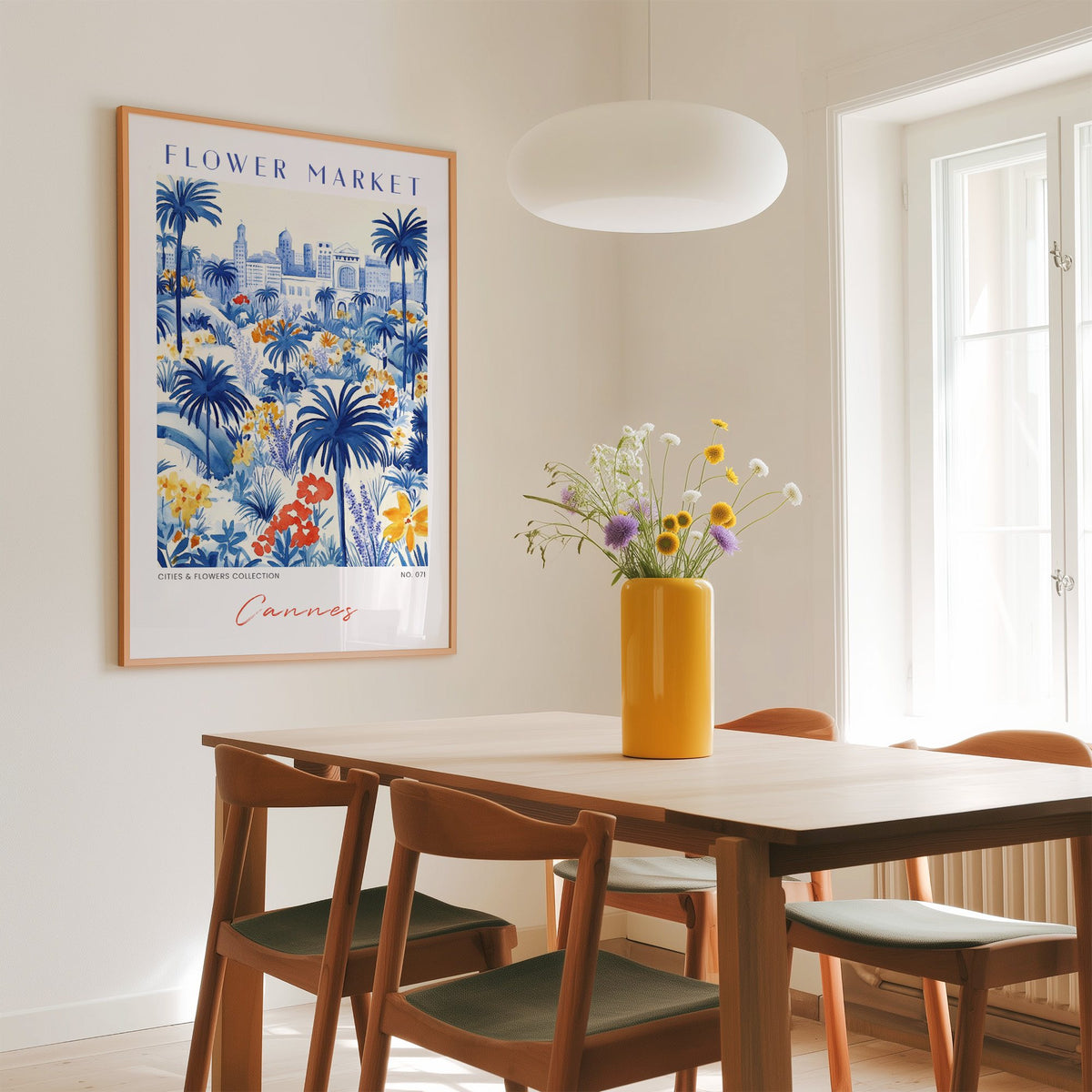 Cannes flower market print in an oak frame above a dining table with a yellow vase and white pendant light
