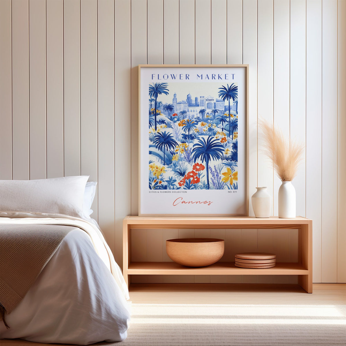 Cannes flower market print in an oak frame on a wood bench against a white shiplap bedroom wall with pampas grass