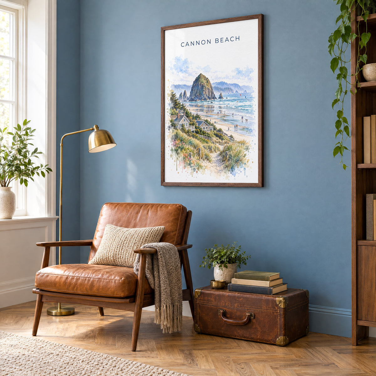 Cannon Beach watercolor print in a walnut frame on a blue wall above a leather armchair in a reading nook
