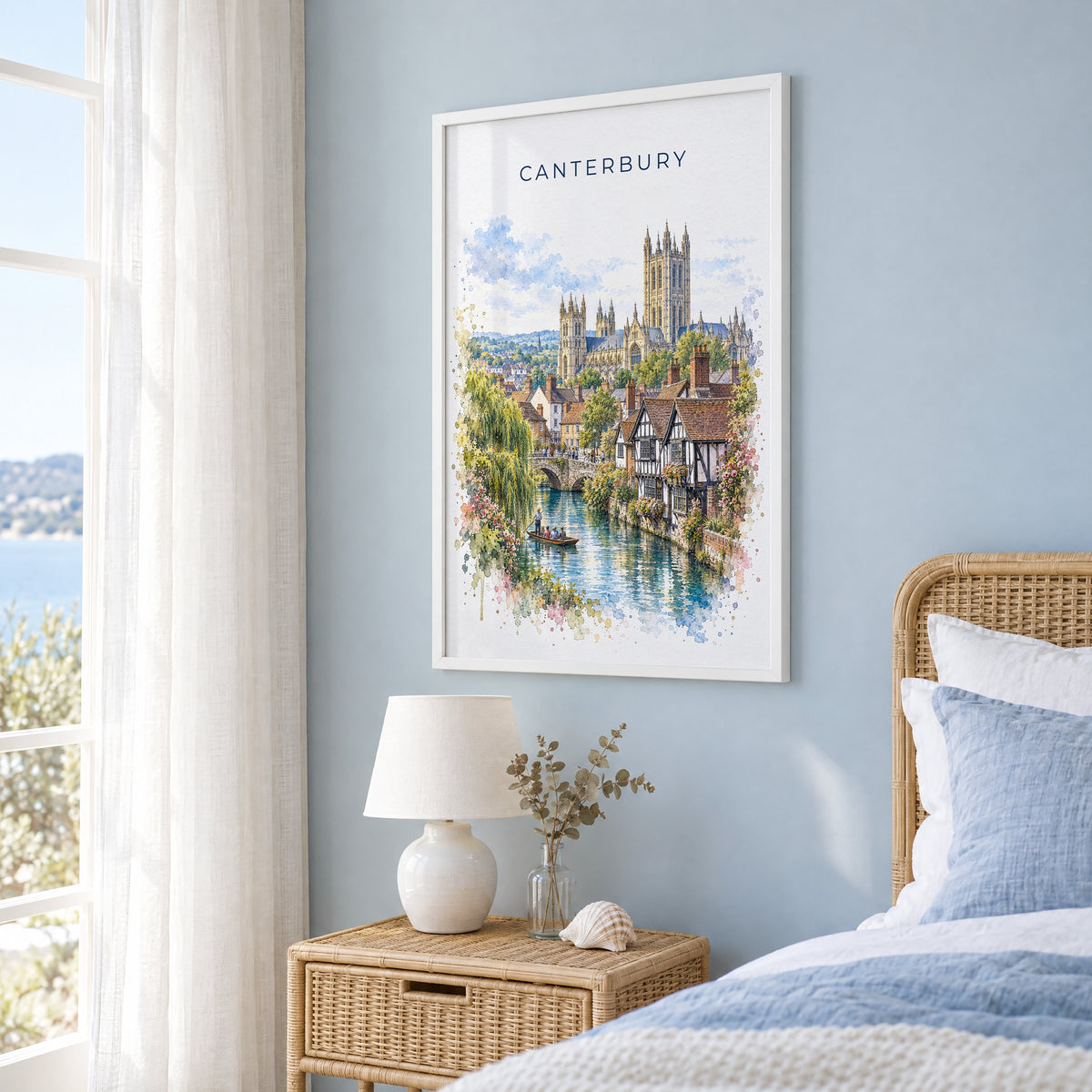 Canterbury, England watercolor print in a white frame on a pale blue wall beside a rattan bed in a coastal bedroom