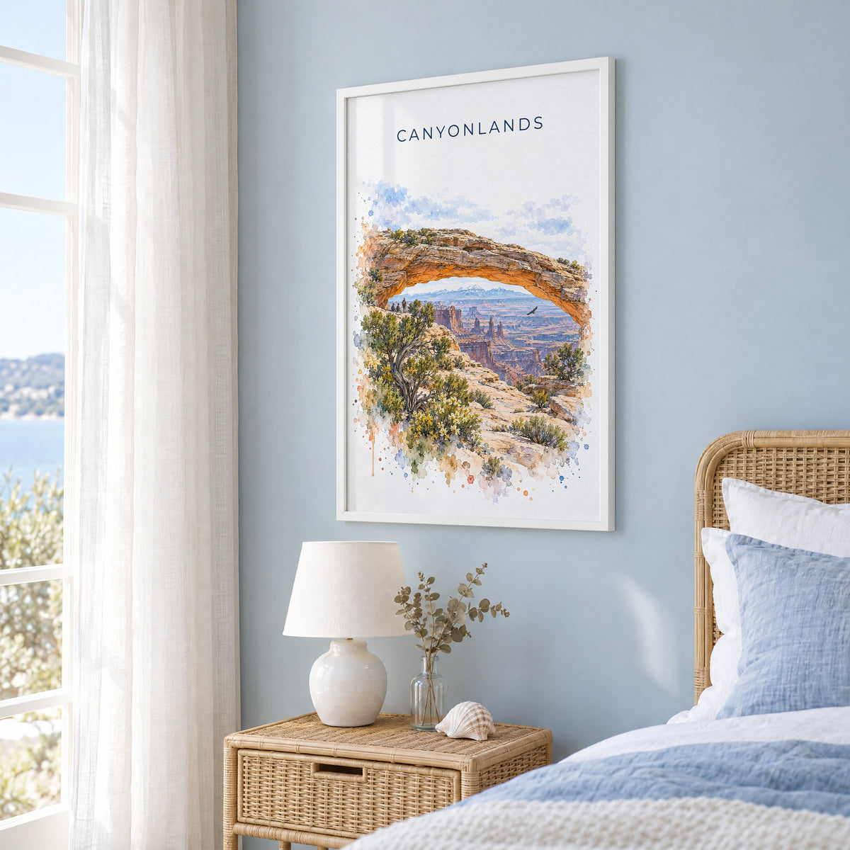 Canyonlands National Park watercolor print in a white frame on a pale blue wall beside a rattan bed in a coastal bedroom