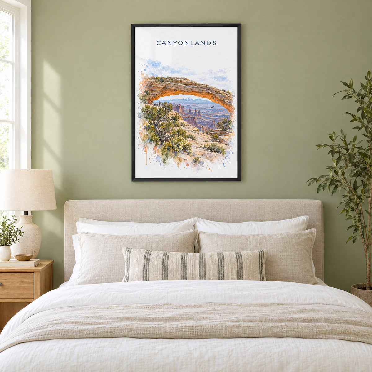 Canyonlands National Park watercolor print in a black frame above an upholstered headboard in a sage green bedroom