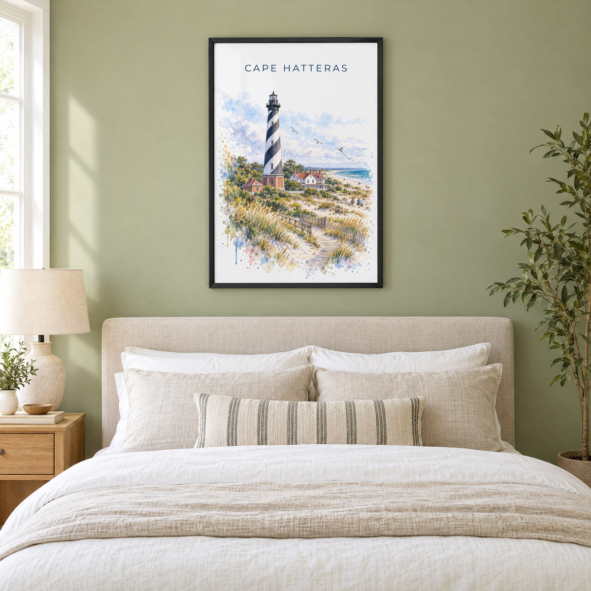 Cape Hatteras watercolor print in a black frame above an upholstered headboard in a sage green bedroom