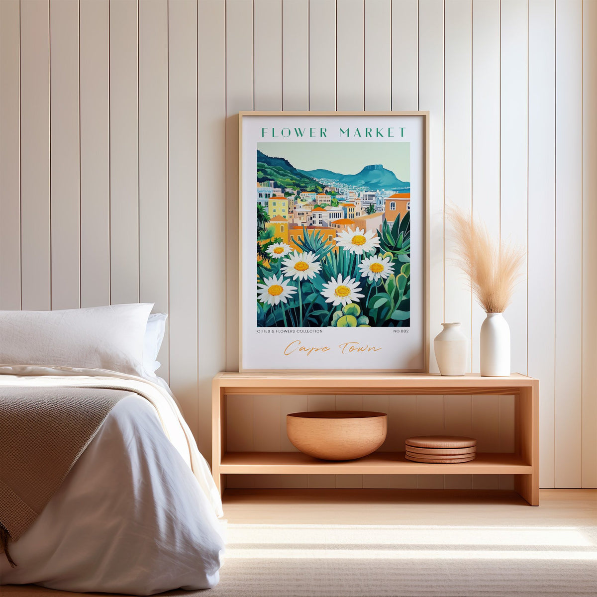 Cape Town flower market print in an oak frame on a wood bench against a white shiplap bedroom wall with pampas grass