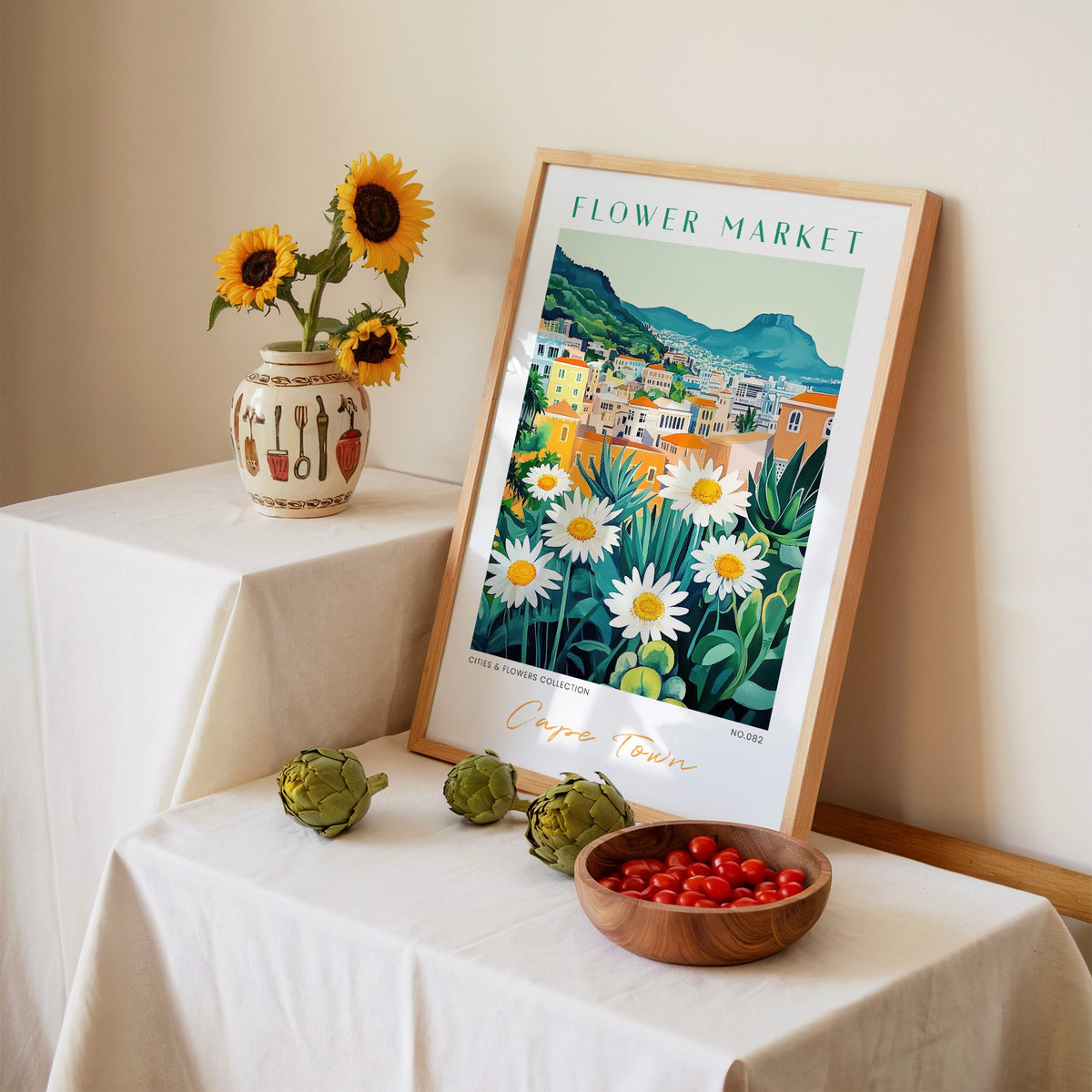 Cape Town flower market print in an oak frame leaning on a linen-draped table beside a vase of sunflowers