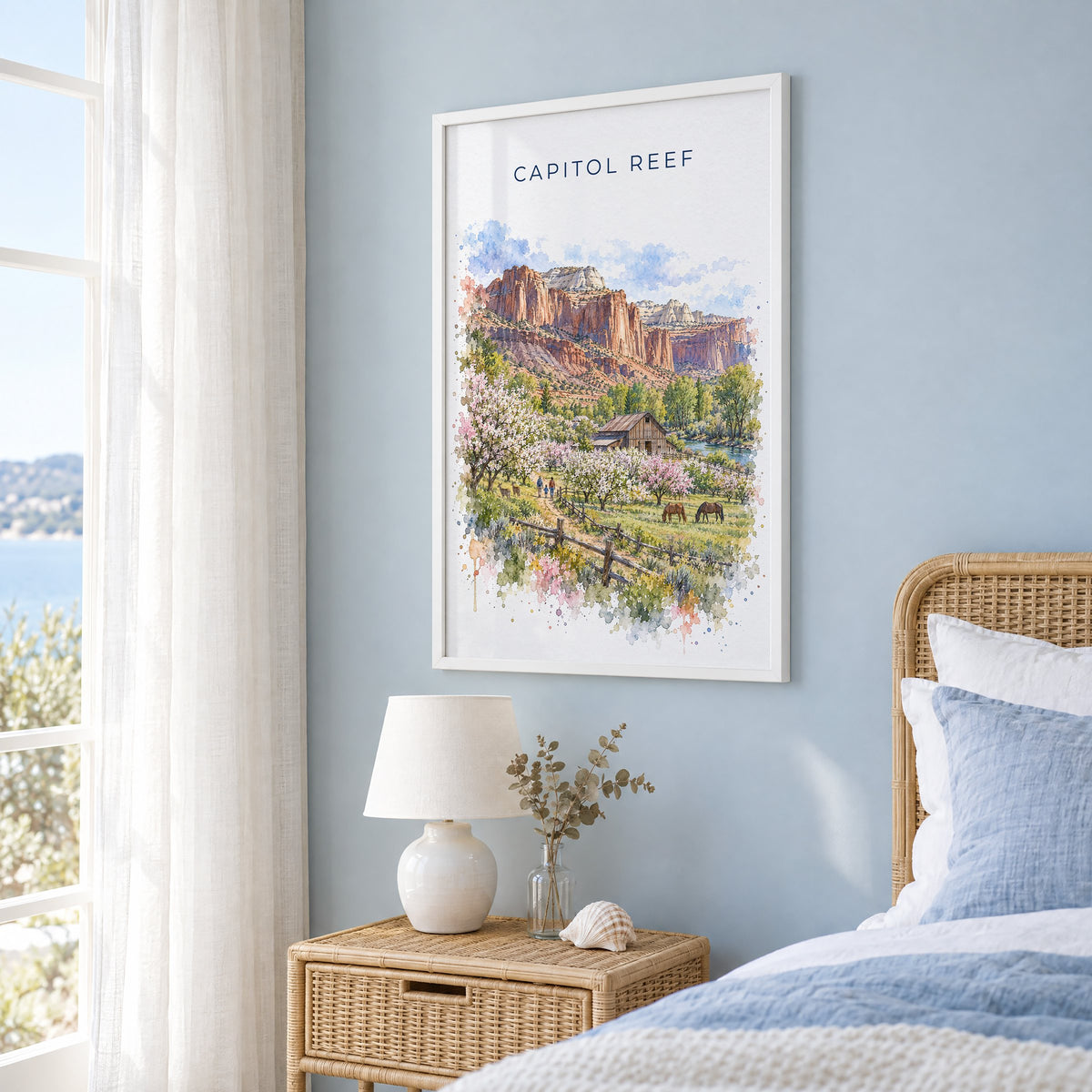 Capitol Reef National Park watercolor print in a white frame on a pale blue wall beside a rattan bed in a coastal bedroom