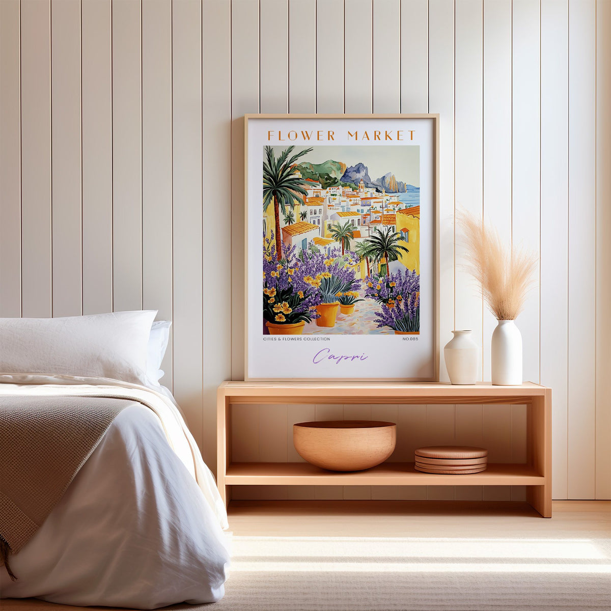 Capri flower market print in an oak frame on a wood bench against a white shiplap bedroom wall with pampas grass