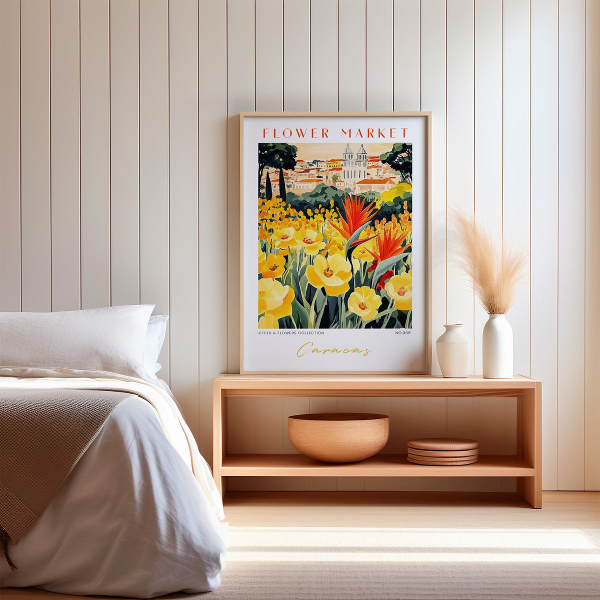 Caracas flower market print in an oak frame on a wood bench against a white shiplap bedroom wall with pampas grass