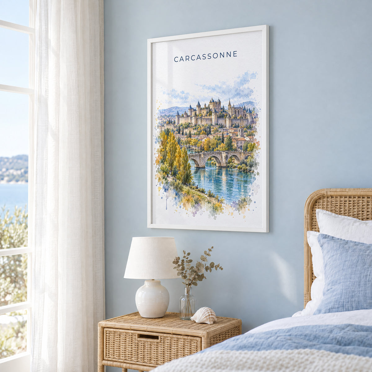 Carcassonne watercolor print in a white frame on a pale blue wall beside a rattan bed in a coastal bedroom