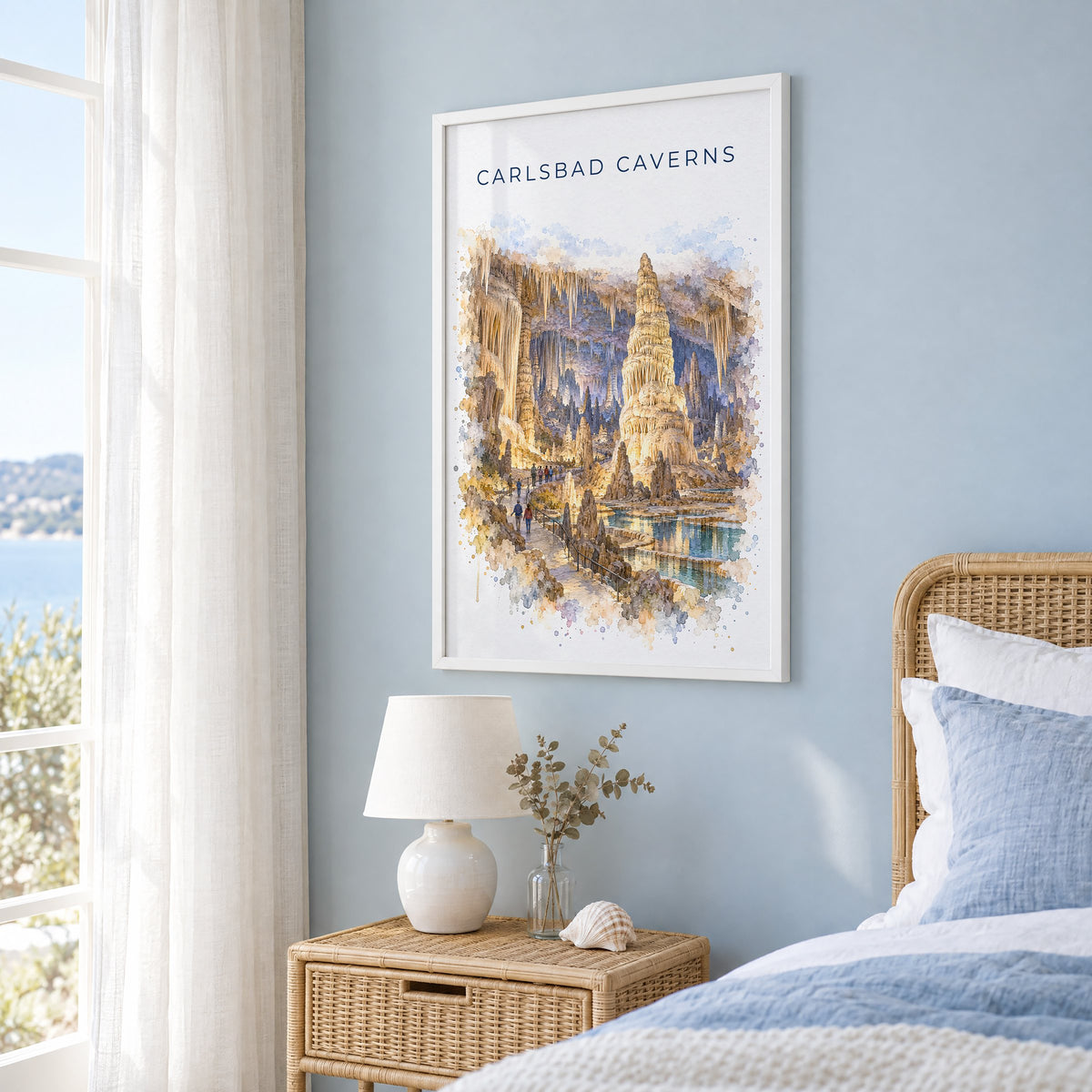 Carlsbad Caverns National Park watercolor print in a white frame on a pale blue wall beside a rattan bed in a coastal bedroom