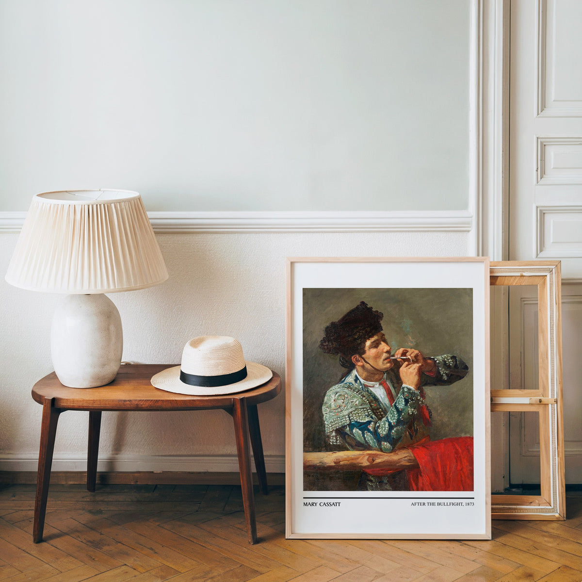 Spanish impressionist poster in a light wood frame leaning by a bench and hat