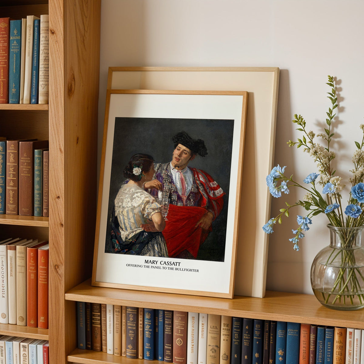 Seville scene print in an oak frame leaning on a bookshelf beside flowers
