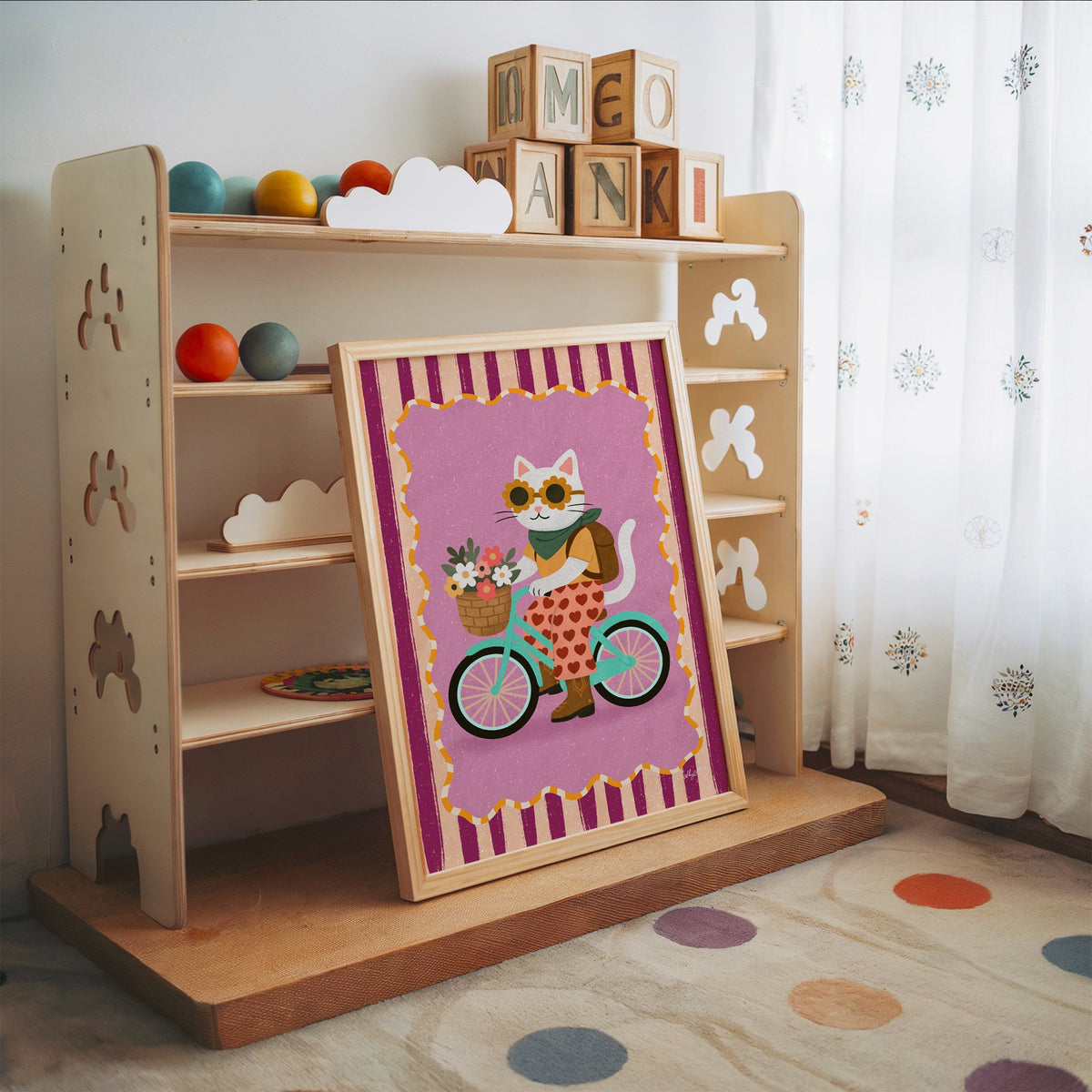 White cat riding a mint bicycle nursery print in an oak frame leaning on a toy shelf with wooden letter blocks