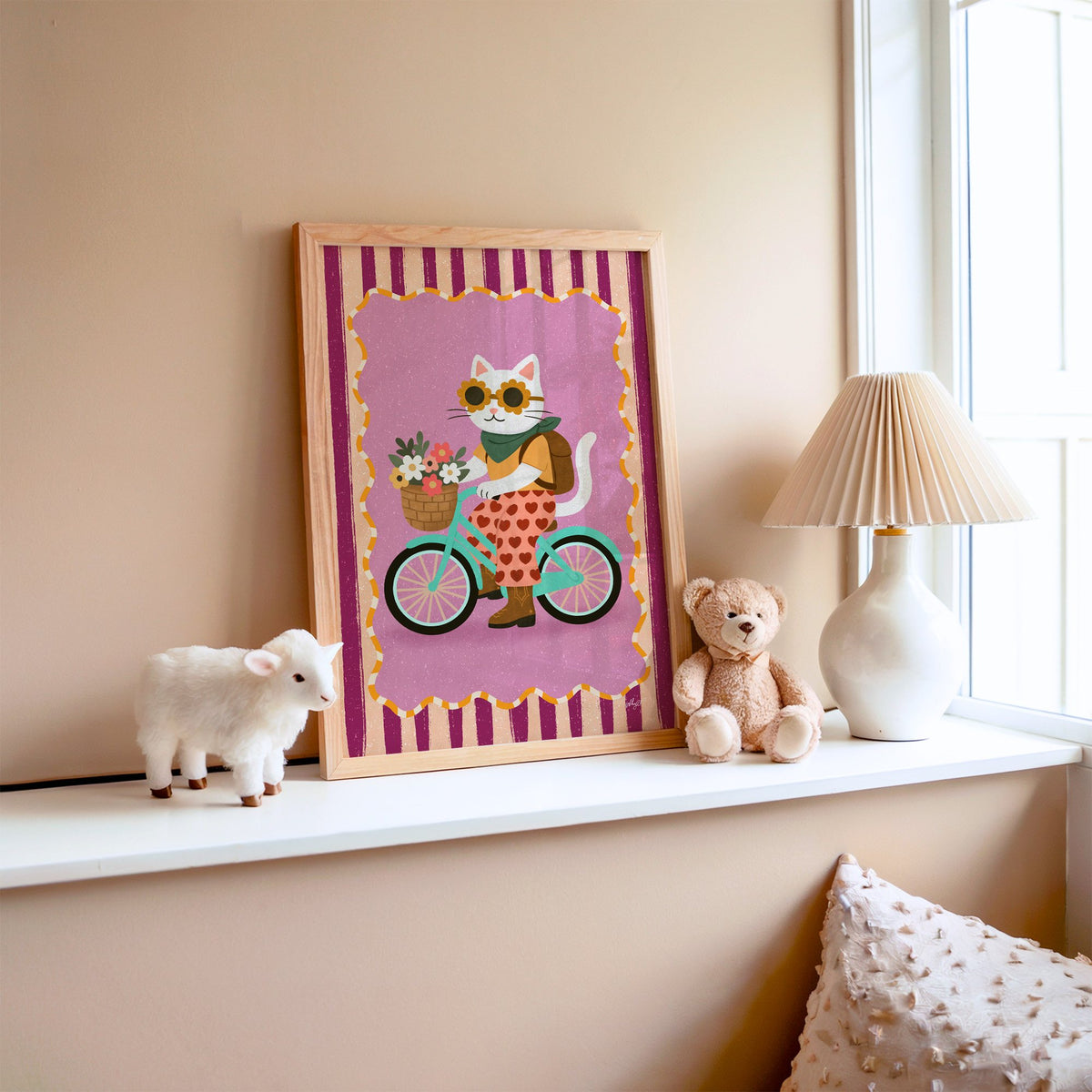 White cat riding a mint bicycle nursery print in an oak frame on a window ledge with a toy lamb and teddy