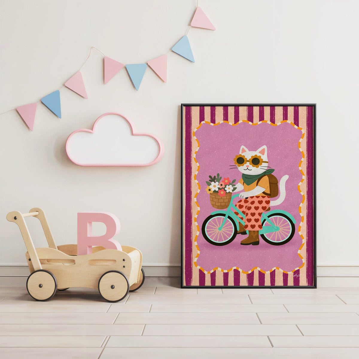 White cat riding a mint bicycle nursery print in a black frame under pastel bunting by a wooden baby walker