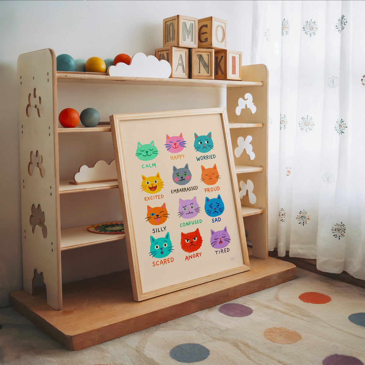 Colourful cat feelings chart nursery print in an oak frame leaning on a toy shelf with wooden letter blocks