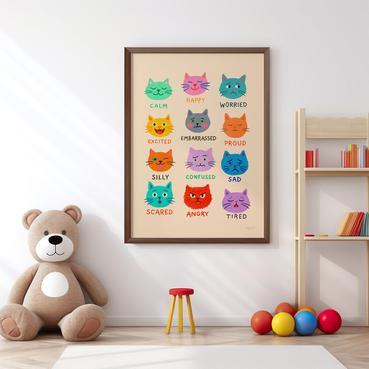 Colourful cat feelings chart nursery print in a walnut frame above a big teddy bear by a bookshelf