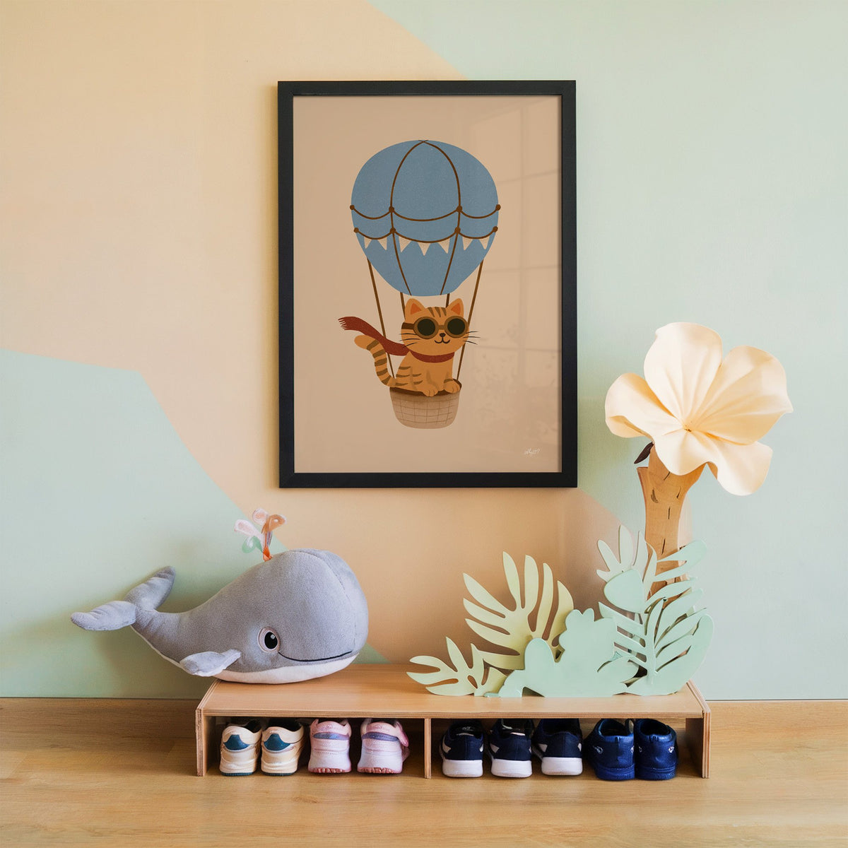 Cat in blue hot air balloon nursery print in a black frame on a mint and peach wall above a whale plush