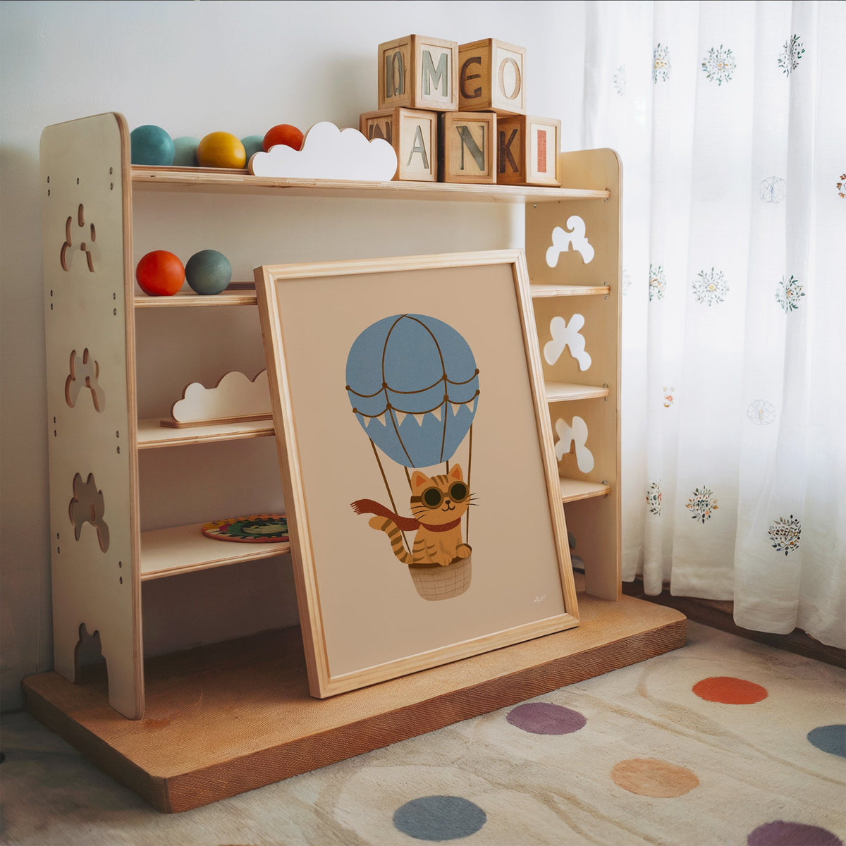 Cat in blue hot air balloon nursery print in an oak frame leaning on a toy shelf with wooden letter blocks