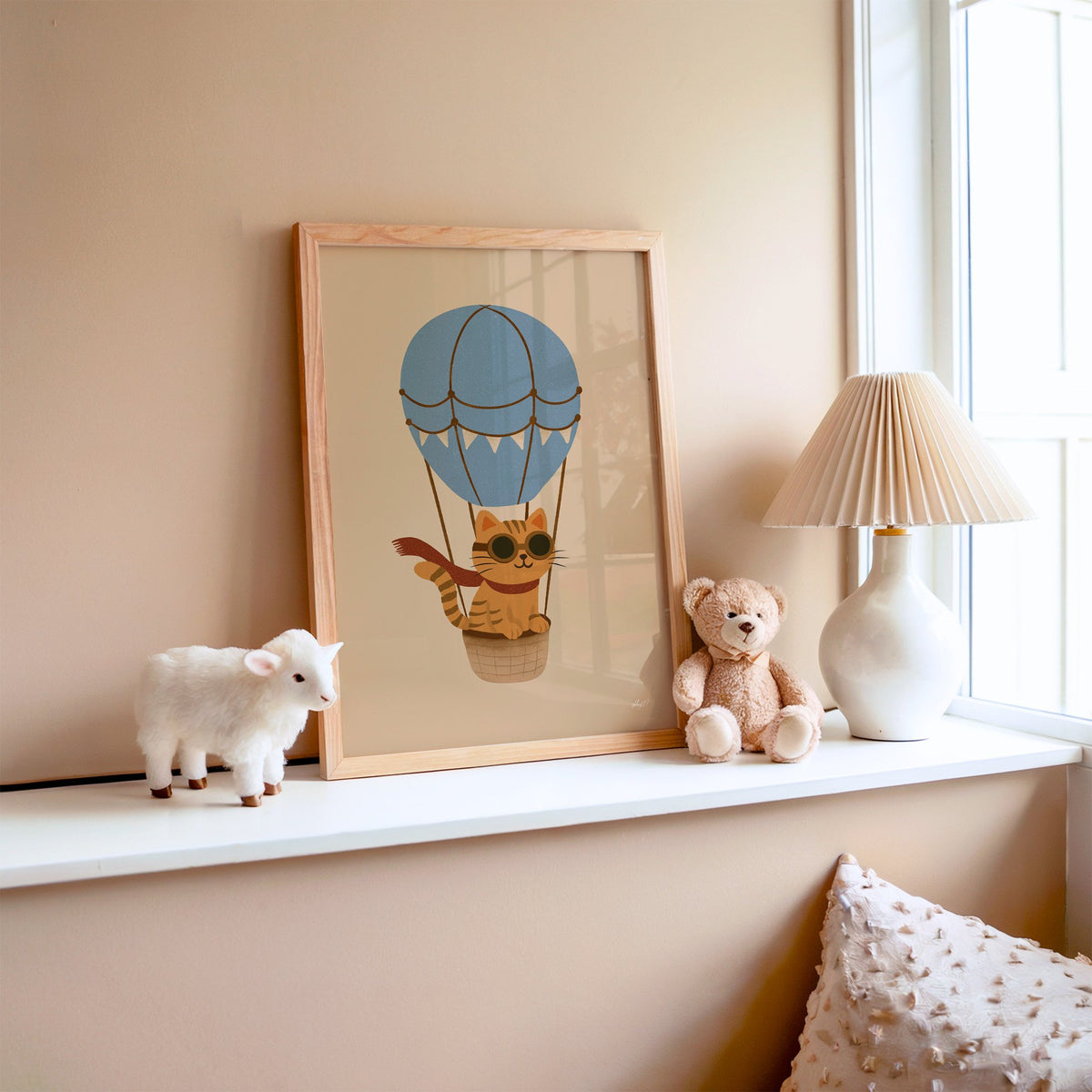 Cat in blue hot air balloon nursery print in an oak frame on a window ledge with a toy lamb and teddy