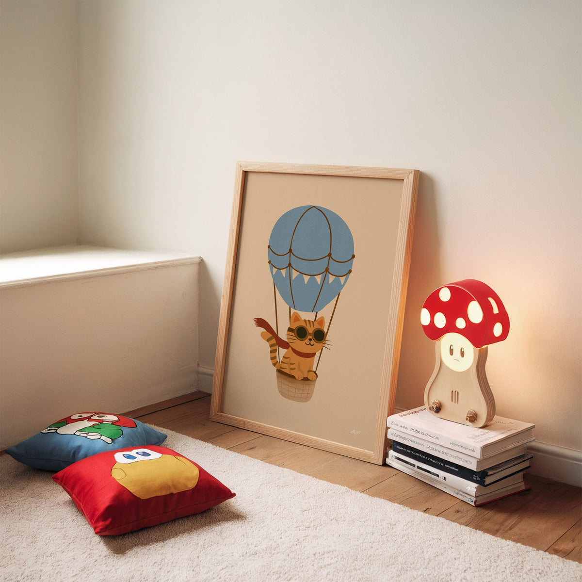Cat in blue hot air balloon nursery print in an oak frame leaning on a rug beside a mushroom lamp and floor cushions