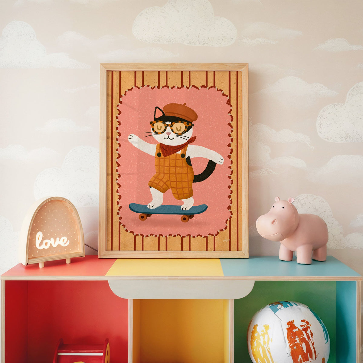 Black and white cat on skateboard nursery print in an oak frame on a rainbow toy shelf against cloud wallpaper