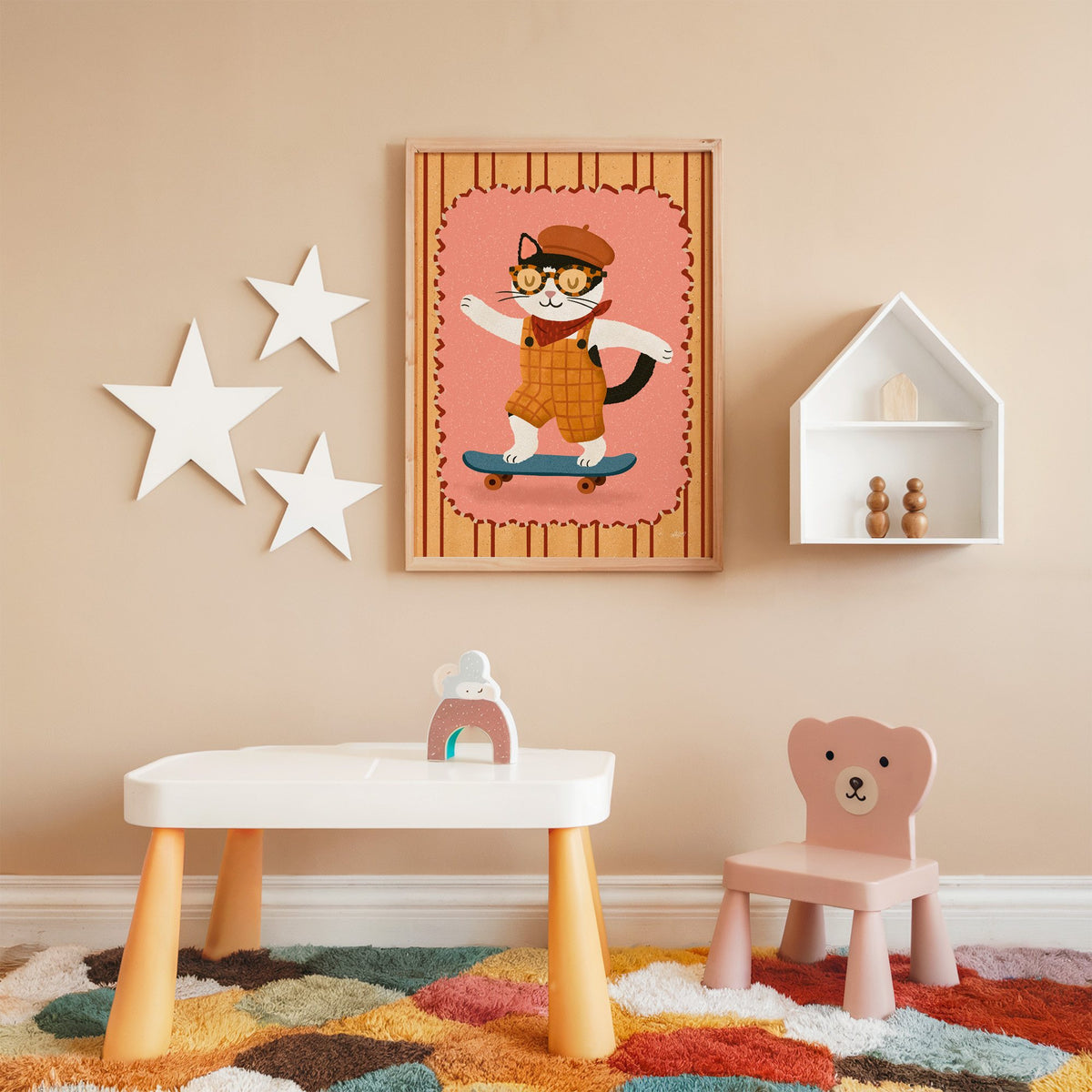 Black and white cat on skateboard nursery print in an oak frame on a peach wall above a kids table with wall stars