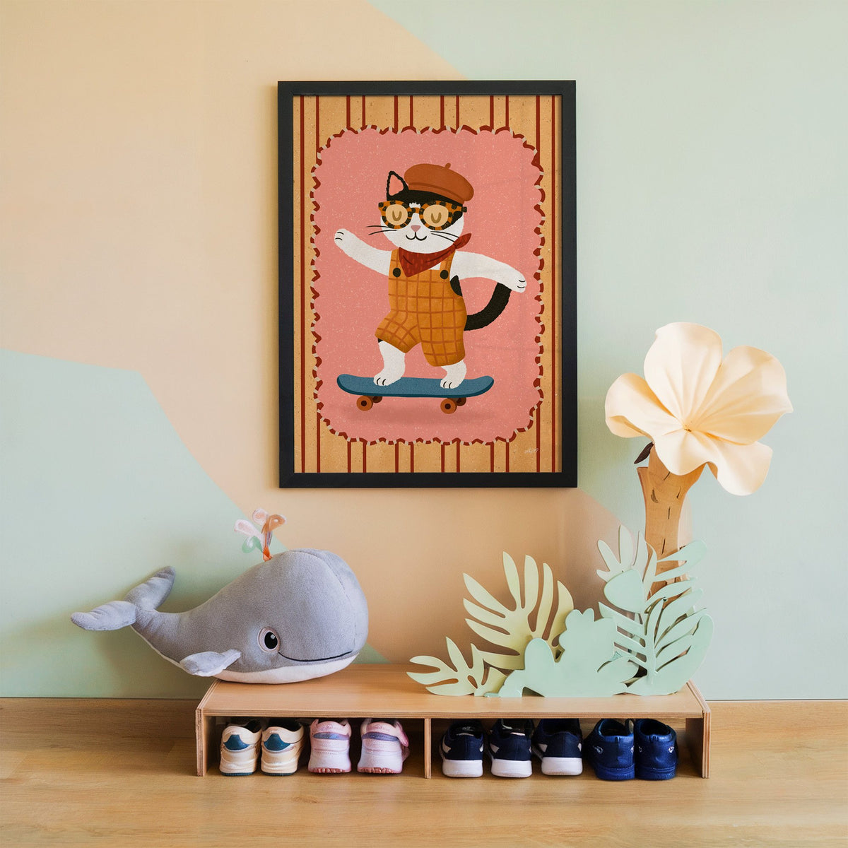 Black and white cat on skateboard nursery print in a black frame on a mint and peach wall above a whale plush