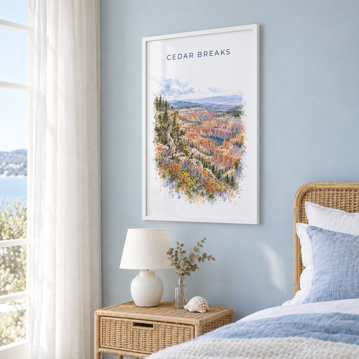 Cedar Breaks National Monument watercolor print in a white frame on a pale blue wall beside a rattan bed in a coastal bedroom