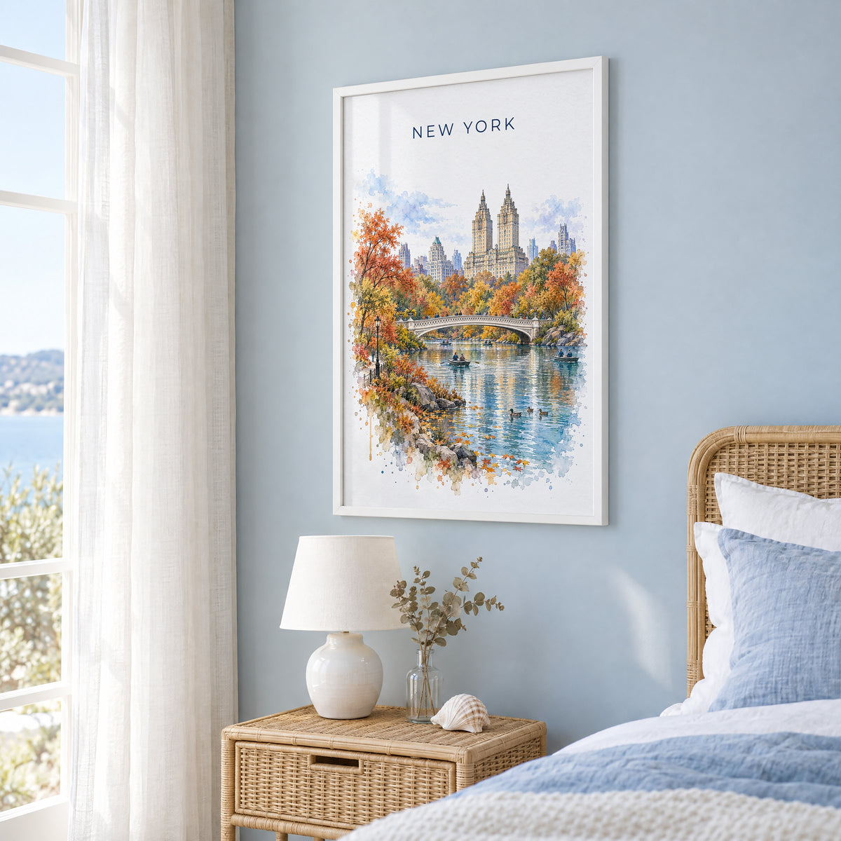 Central Park watercolor print in a white frame on a pale blue wall beside a rattan bed in a coastal bedroom