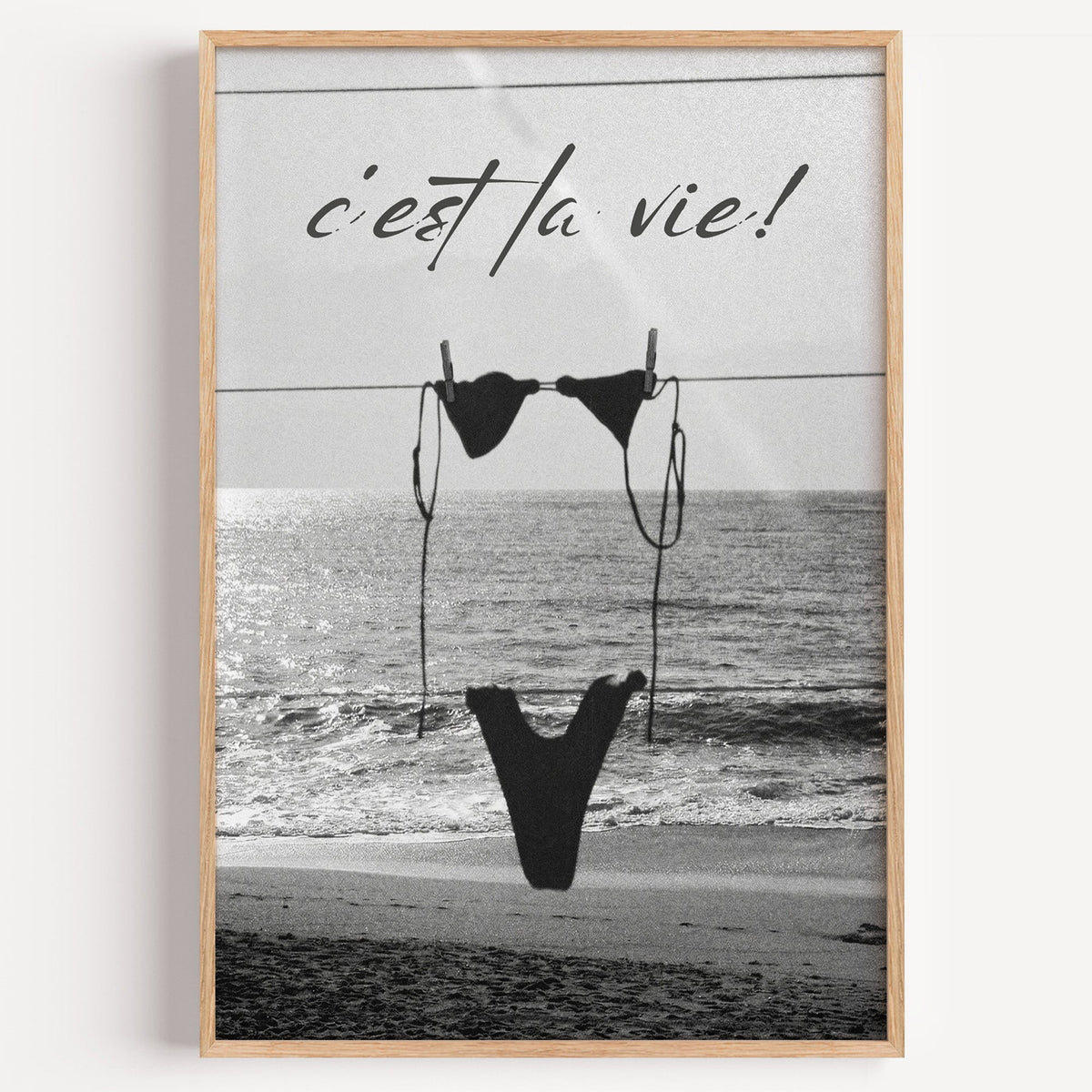 Black bikini on a clothesline over the sea print in a light oak frame on a plain white wall