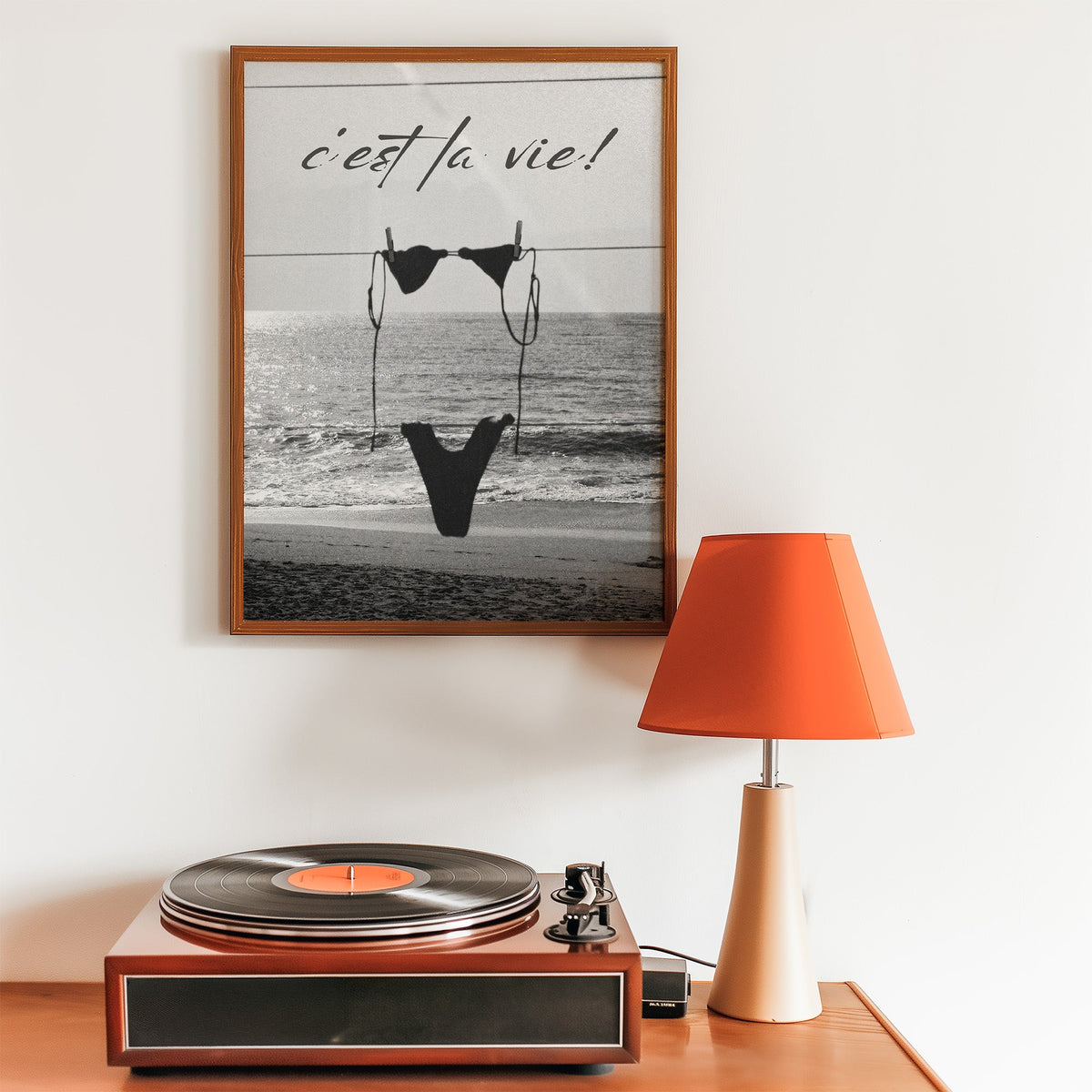 Black bikini on a clothesline over the sea print in a walnut frame above a record player and orange lamp