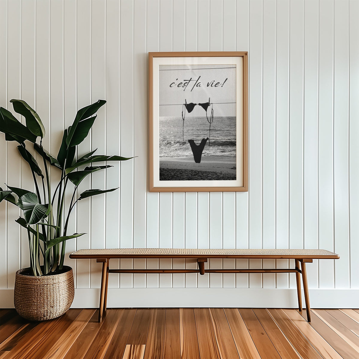Black bikini on a clothesline over the sea print in a wood frame with a white mat above a cane bench
