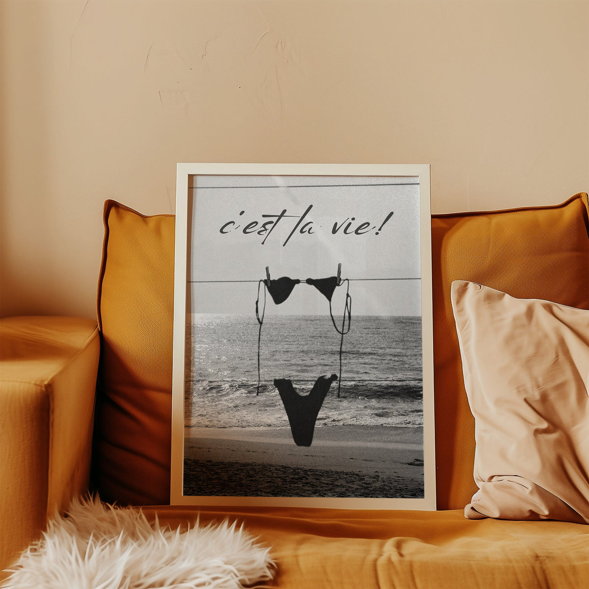 Black bikini on a clothesline over the sea print in a white frame leaning on a mustard velvet sofa