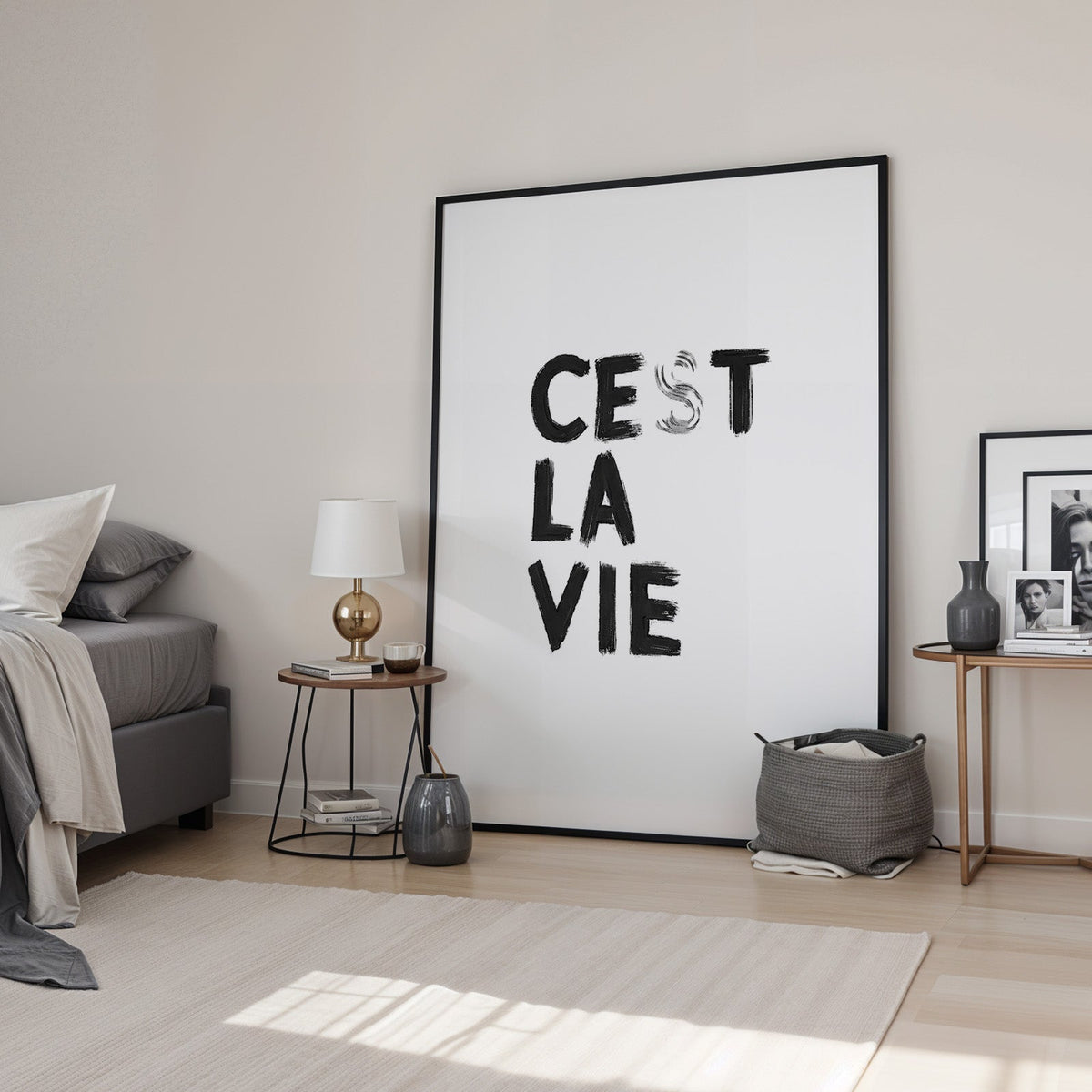 Cest la vie brush lettering on white print in a black frame leaning in a bedroom beside a gold lamp