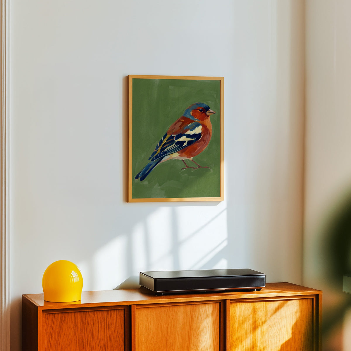 Garden bird wall art print in a light oak frame above a teak sideboard with a yellow lamp