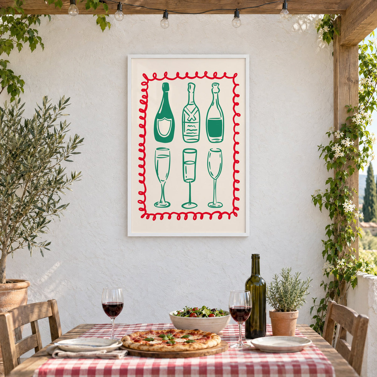 Green champagne bottles and glasses squiggle frame print in a white frame on a stucco wall above a checked-cloth table with pizza and red wine