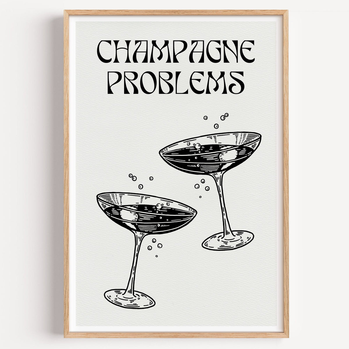 Champagne Problems engraved coupes print in a light oak frame on a plain white wall