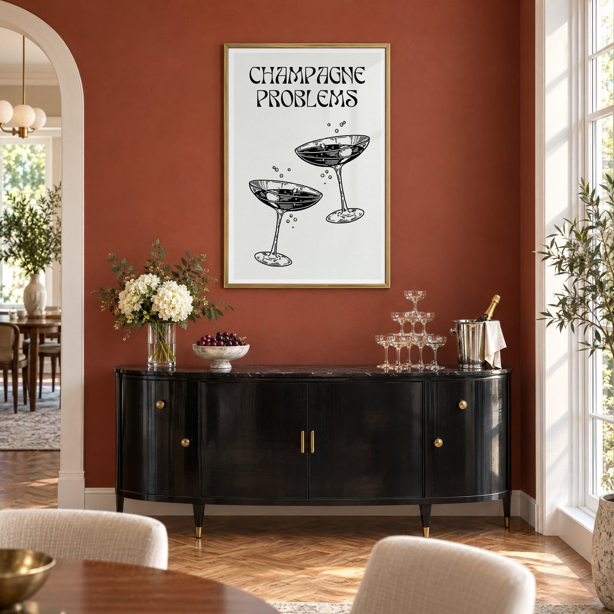Champagne Problems engraved coupes print in a brass frame on a terracotta wall above a black buffet with a champagne tower