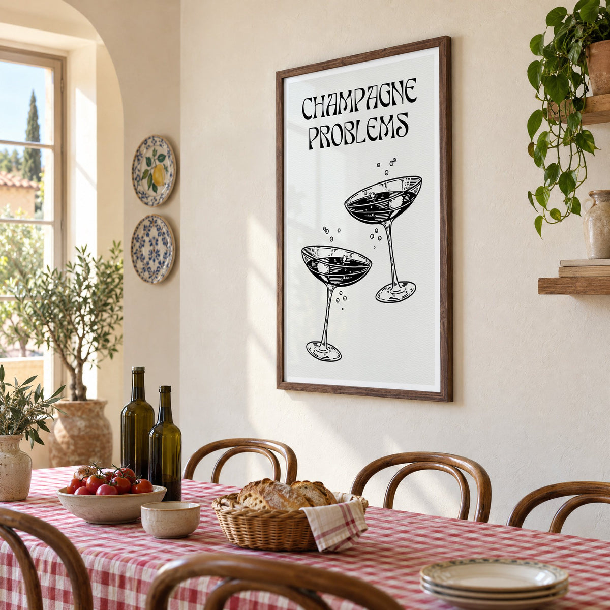 Champagne Problems engraved coupes print in a walnut frame above a gingham-covered trattoria table, seen at an angle