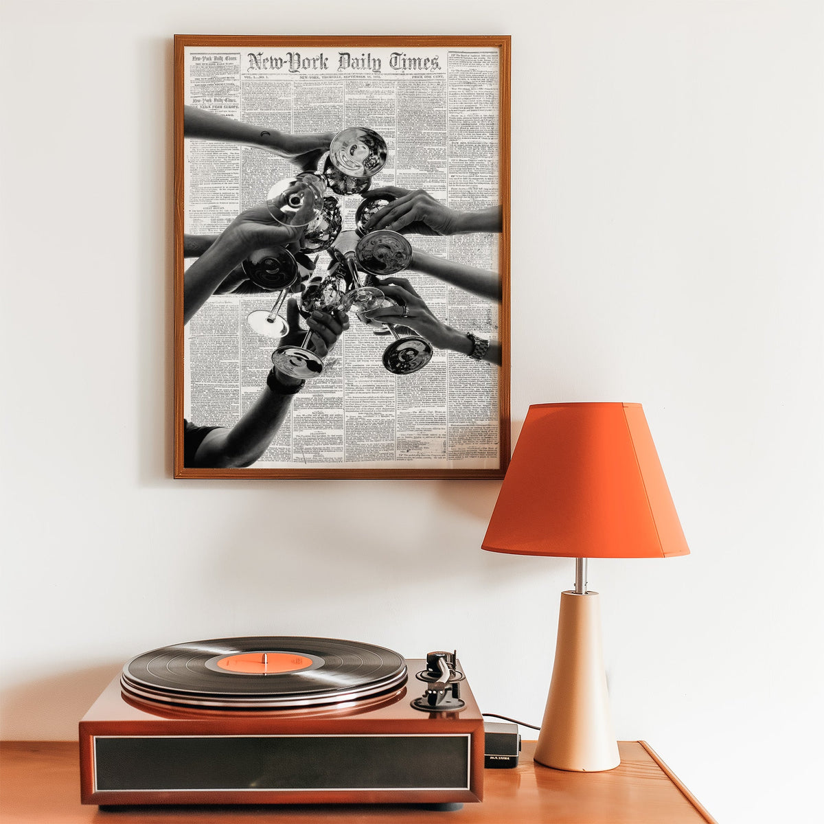 Champagne toast collage on 1851 newspaper print in a walnut frame above a record player and orange lamp