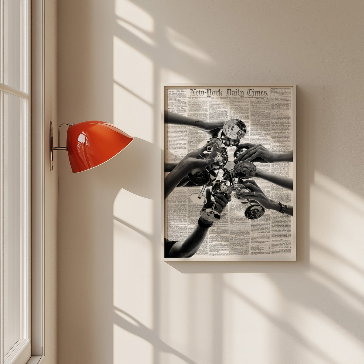 Champagne toast collage on 1851 newspaper print in a white frame on a sunlit wall beside a red sconce